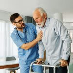 A nurse helping a man with stroke rehabilitation using a walker.