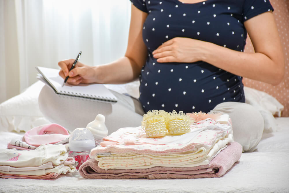 Mum making a check list and organising the baby clothes while rubbing her pregnant belly