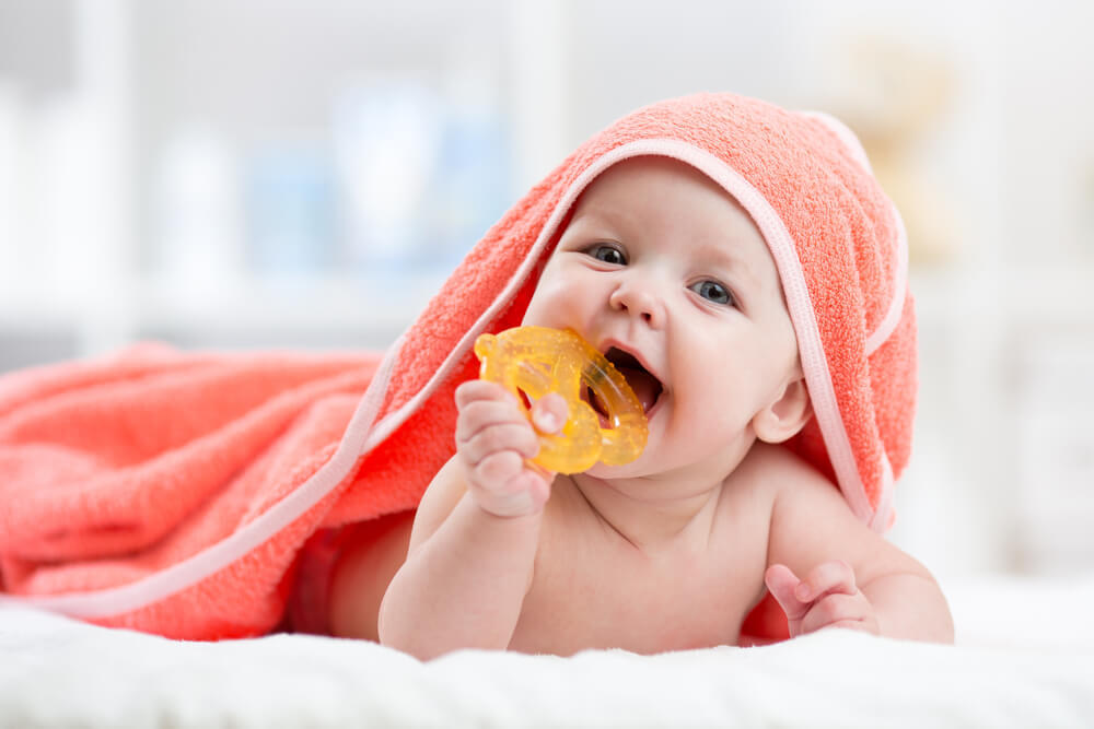 Baby wrapped in a towel chewing on a teething toy