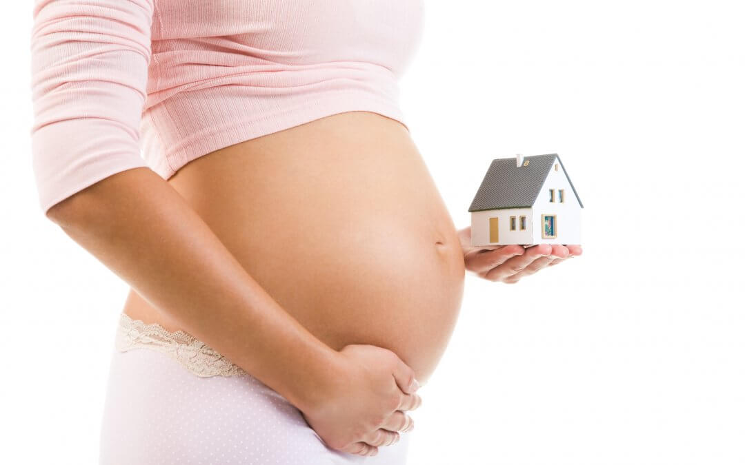 pregnant lady holding a small house next to her baby bump