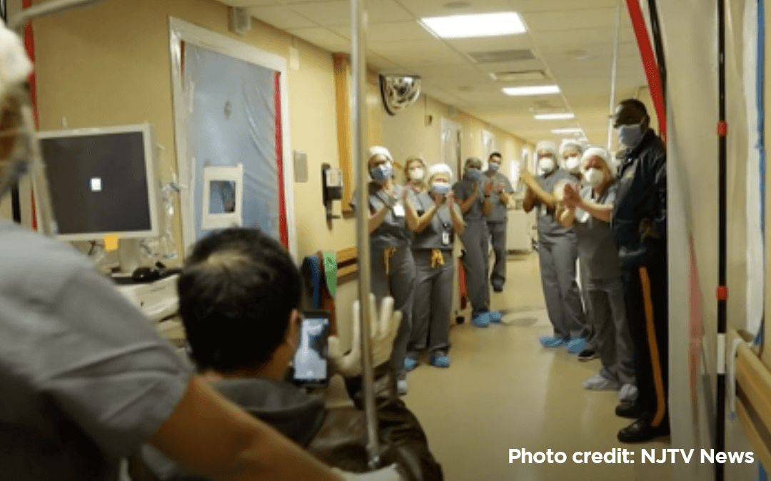 Corridor in a hospital with a patient being wheeled in a chair while doctors and nurses applaud