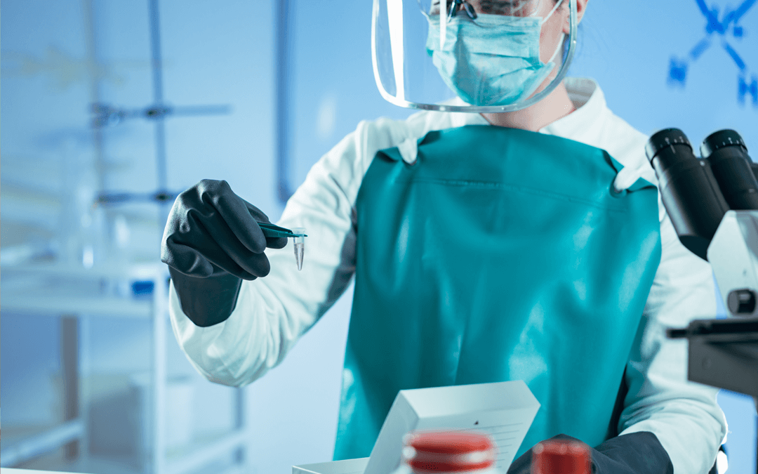 Lab tech in full PPC carrying a small vial with a pair of tweezers