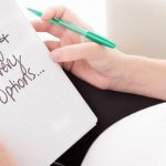 Pregnant woman holding a green pen and a notepad with the words 'birthing & delivery options' hand written on the page.