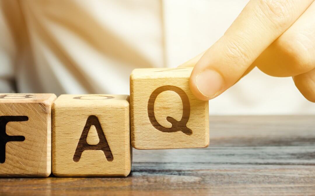 Three wooden building blocks lettered F A Q with a hand picking up the block with the letter Q.
