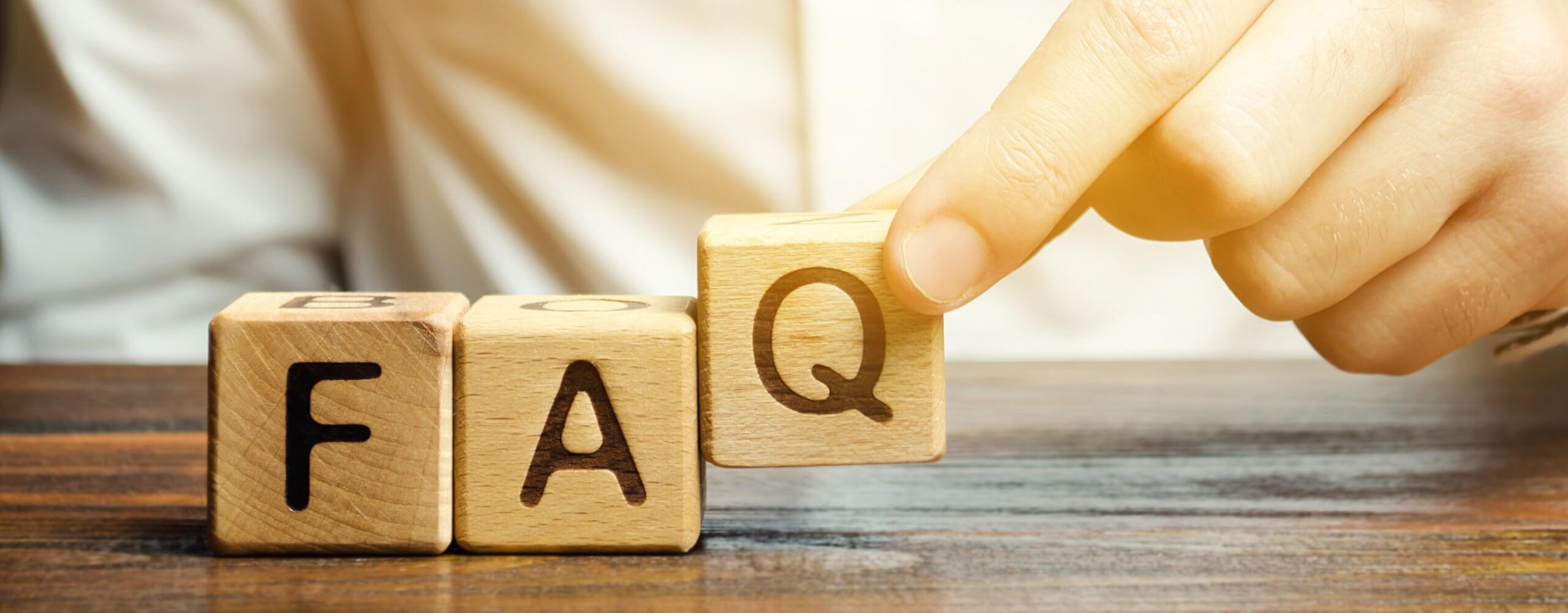 Three wooden building blocks lettered F A Q with a hand picking up the block with the letter Q.