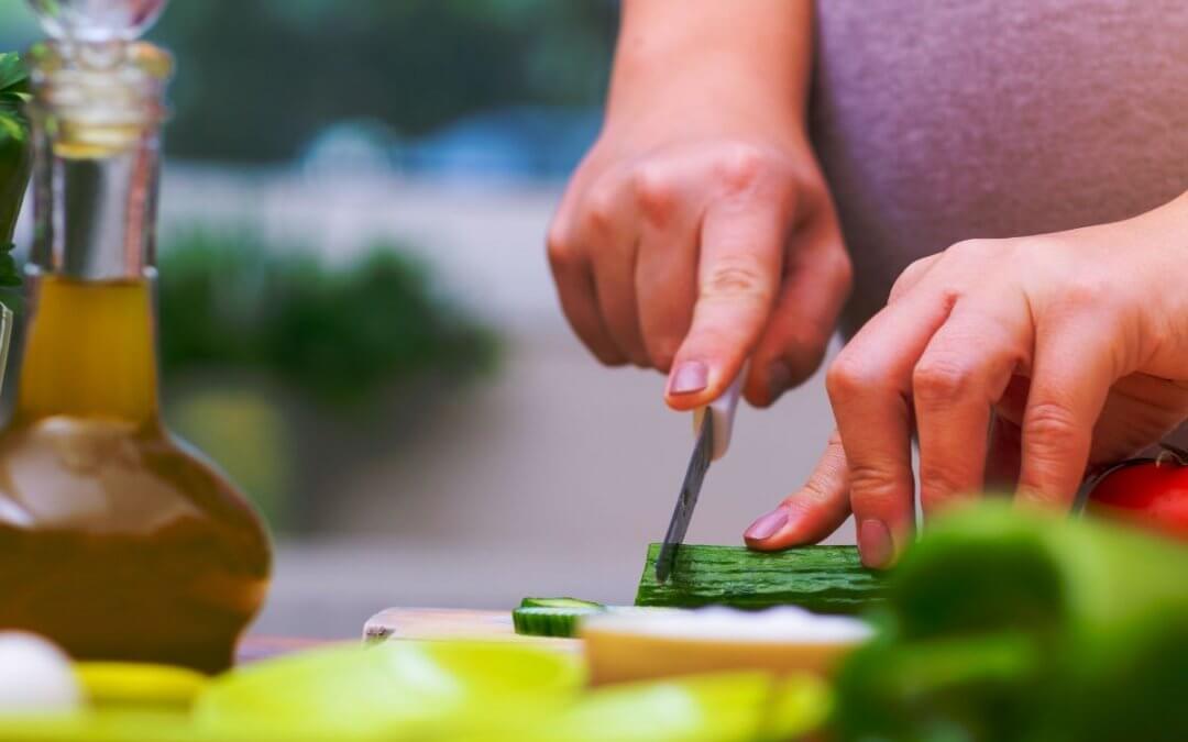 A pregnant woman holding a knife and slicing a cucumber.