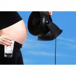 Pregnant woman wearing a black crop top holding a glass of iced water and a cooling fan.