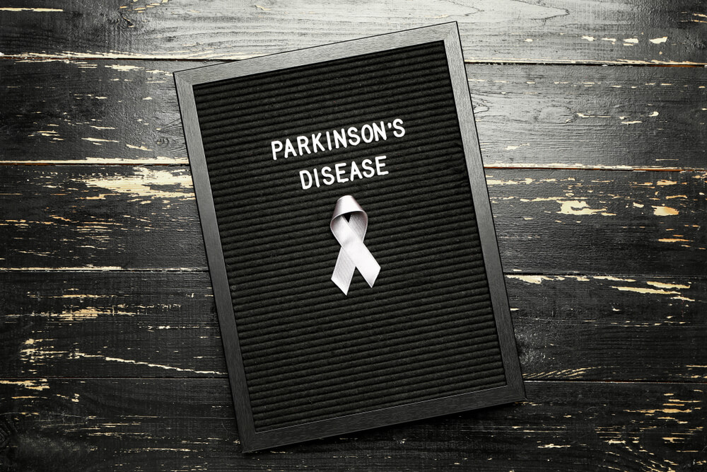 Board with text PARKINSON'S DISEASE and awareness ribbon on dark background