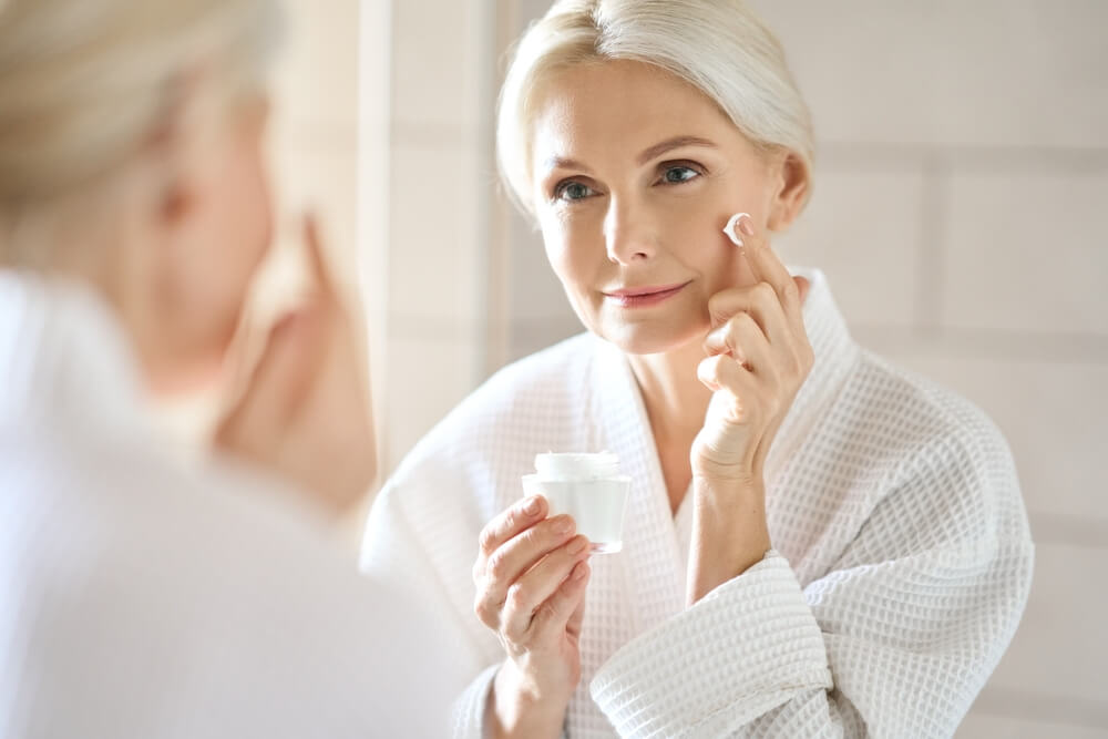 An older lady applies anti-ageing cream while looking in the mirror