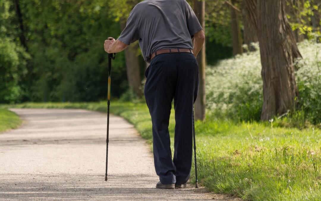 An elderly man walking on a path with walking sticks